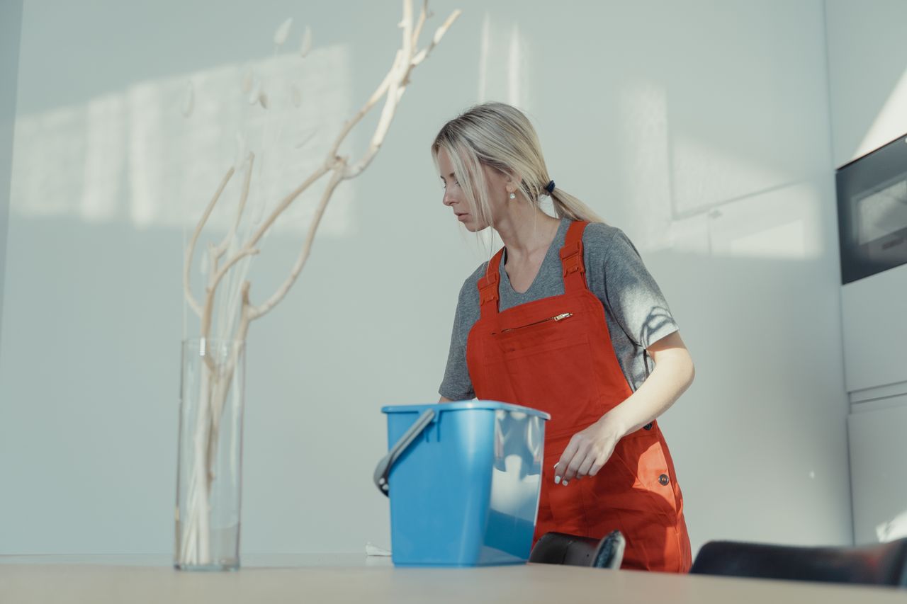 A woman dressed in a red uniform is cleaning inside with a blue bucket, helping maintain a spotless setting.